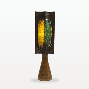 Photographie d'une lampe de la manufacture d'Accolay. L'abat-jour de la lampe est faite en métal est résine colorée. Chaque face de la lampe est d'une couleur différente : ocre, orange, jaune et verte.
