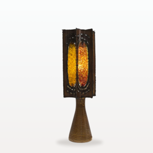 Photographie d'une lampe de la manufacture d'Accolay. L'abat-jour de la lampe est faite en métal est résine colorée. Chaque face de la lampe est d'une couleur différente : ocre, orange, jaune et verte.