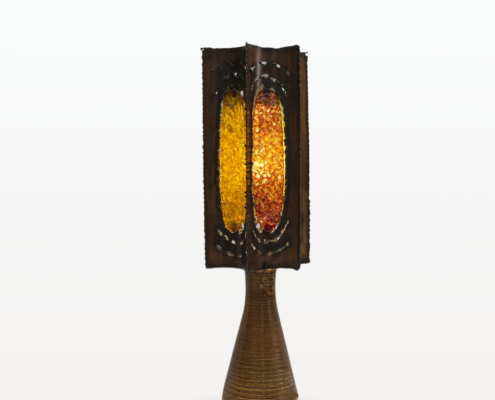 Photographie d'une lampe de la manufacture d'Accolay. L'abat-jour de la lampe est faite en métal est résine colorée. Chaque face de la lampe est d'une couleur différente : ocre, orange, jaune et verte.